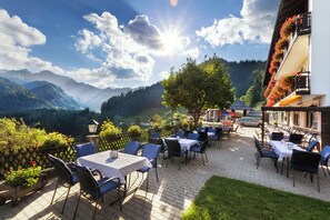 Un patio exterior con mesas y sillas, con vistas a un paisaje montañoso.