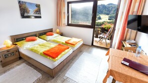A hotel room with two beds, a TV, a desk, and a view of a mountainous landscape. - Bed&Breakfast Lausegger (Ferlach)