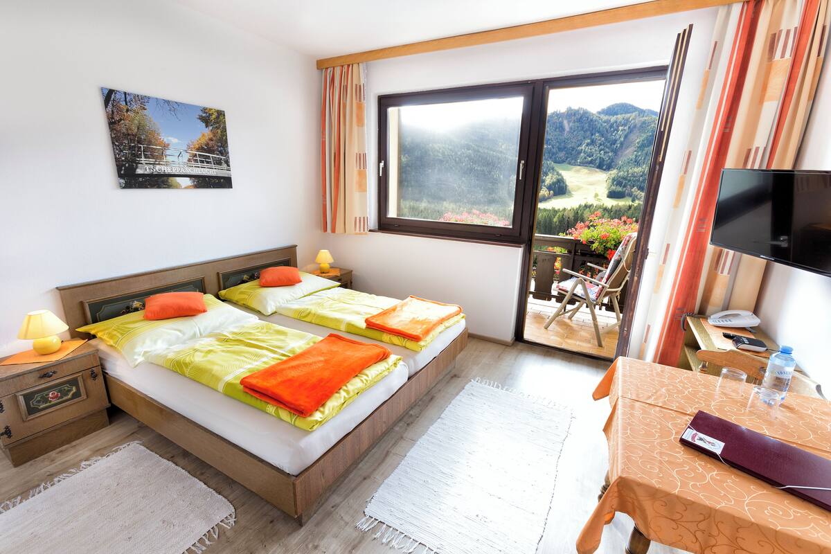 A hotel room with two beds, a TV, a desk, and a view of a mountainous landscape.