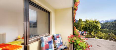 A balcony with a bed, two chairs, and a view of mountains.
