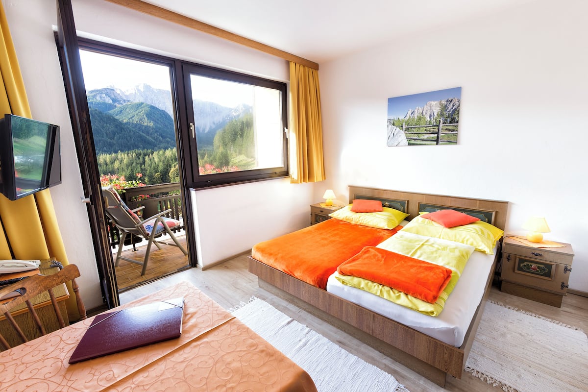 A bedroom with a bed, a desk, a chair, a television, and a window with a mountain view.