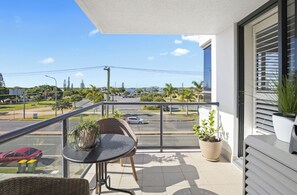 Enjoy the view of the street and palm trees from this balcony, featuring a table and chairs.