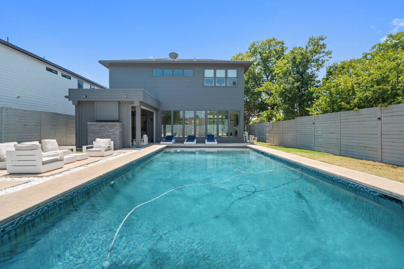 A modern house with a swimming pool, outdoor seating, and a large windowed room.
