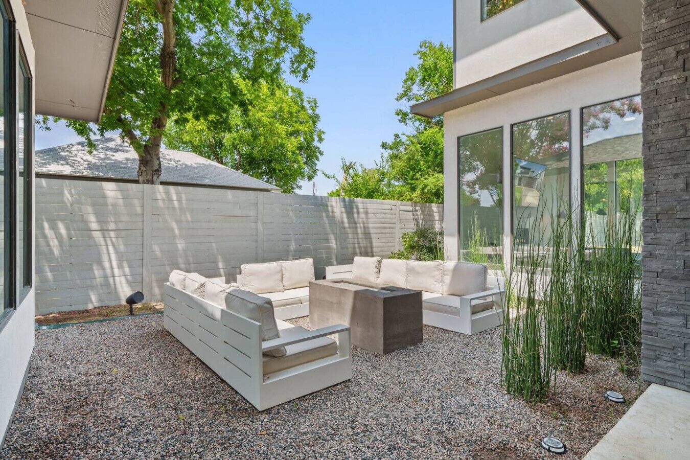 A modern outdoor seating area with a white sofa set, a coffee table, and a stone accent wall.