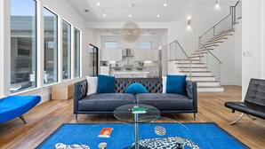 Ein modernes Wohnzimmer mit einem grauen Sofa, blauen Kissen, einem Glastisch und einem blauen Teppich mit Karomuster.