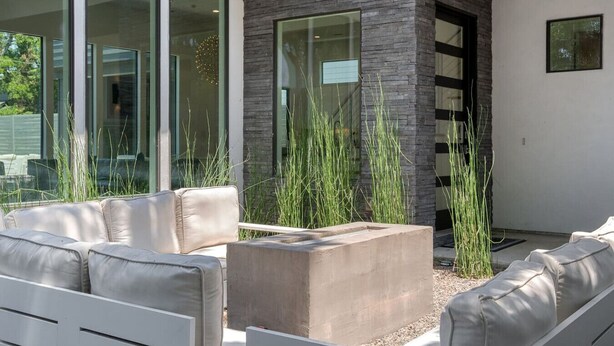 Ein moderner Außenbereich zum Sitzen mit einem Betonpflanzgefäß, wei ßen, gepolsterten Sofas und hohem Gras.