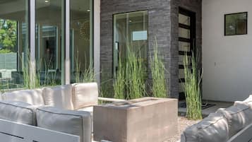 Een modern buitenzitgedeelte met een betonnen plantenbak, witte gestoffeerde banken en hoge grassen.