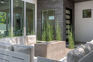 Un espace extérieur moderne, aménagé avec des sièges, comprenant un bac à plantes en béton, des canapés blancs avec des coussins et de hautes herbes.