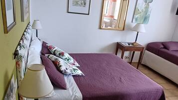 A bedroom with a bed, a bedside table with a lamp, a chair, and a small table with a lamp.