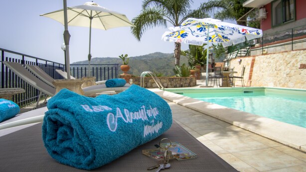 Zona de piscina con una toalla azul, una sombrilla blanca y una pileta.