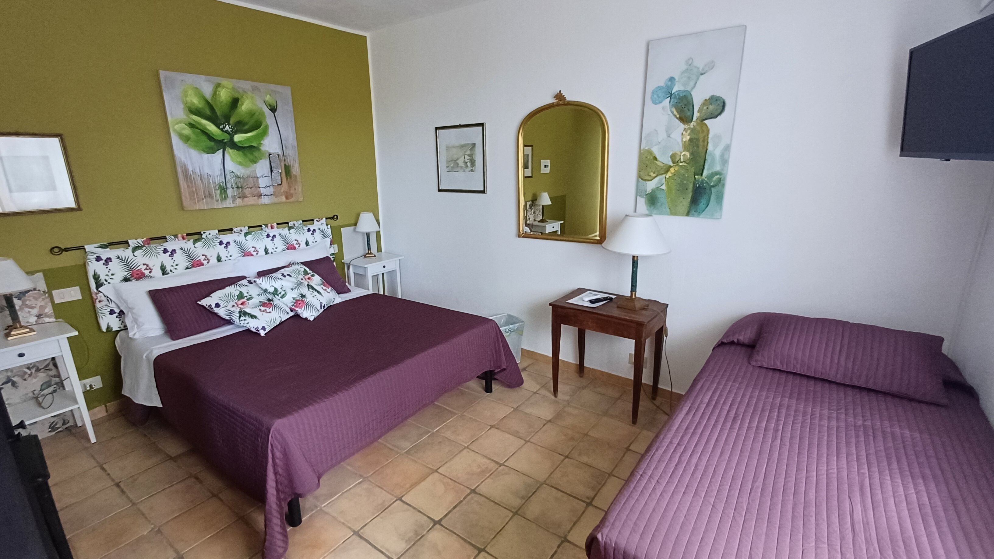 Een hotelkamer met een groot bed, een kleiner bed, een nachtkastje, een lamp en kunstwerken aan de wanden.
