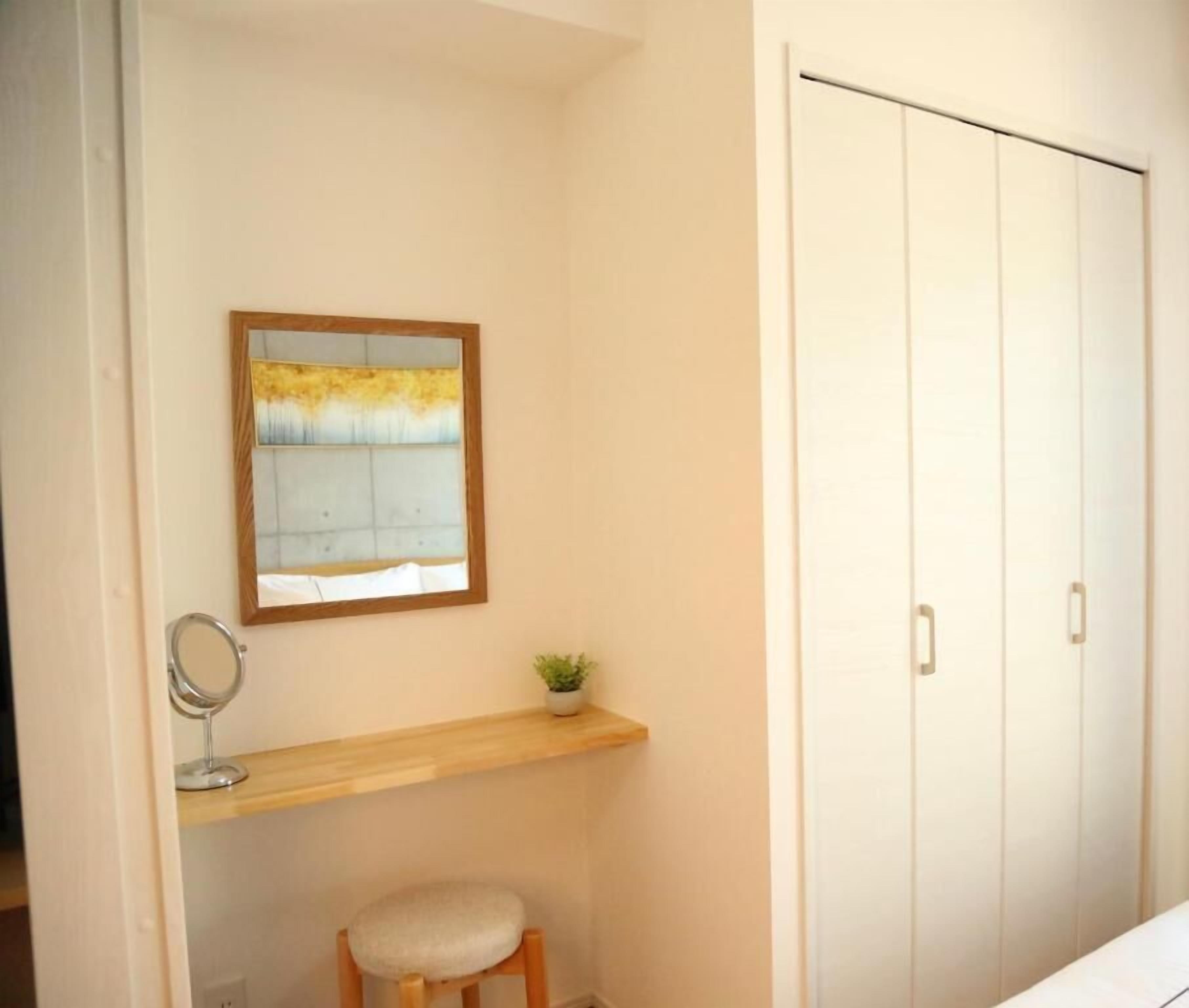 A bathroom with a wooden vanity, a mirror, a stool, a potted plant, and a white wardrobe.