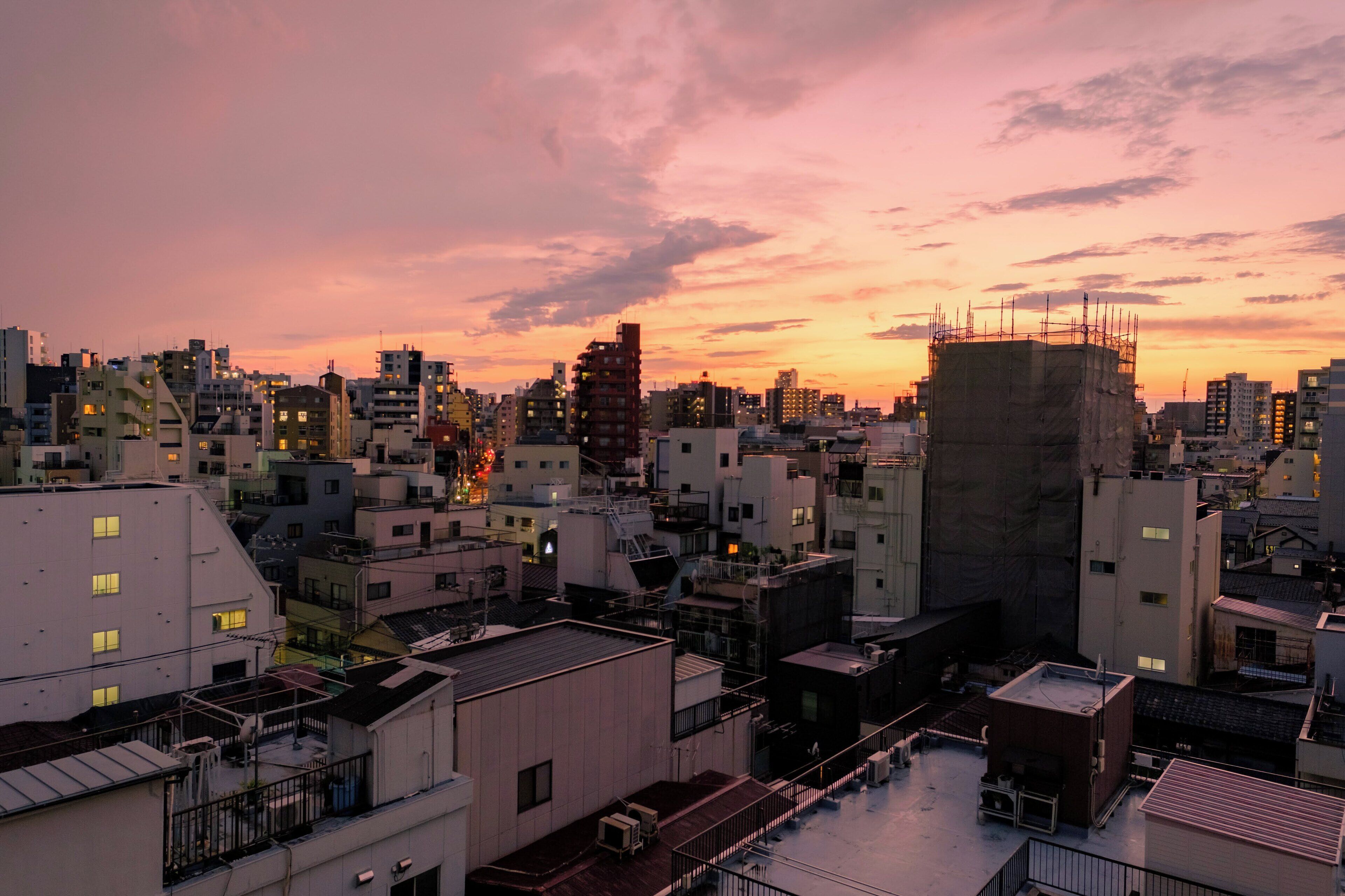 A cityscape at sunset with various buildings, including a construction site with scaffolding.