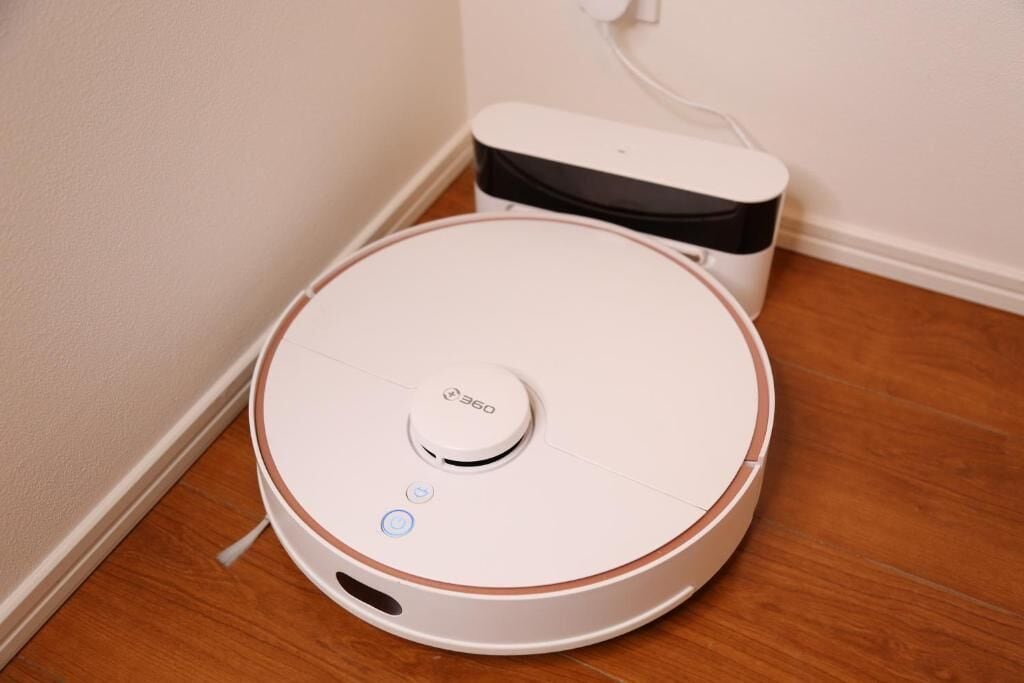 A white robotic vacuum cleaner with a black top, a control button, and a charging dock.