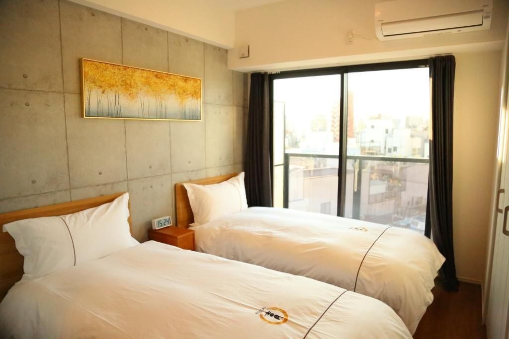 A hotel room with two beds, a painting on the wall, and a large window with curtains.