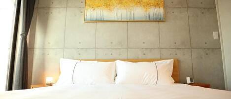 A hotel room with a large bed, a headboard with a textured wall, a painting above the bed, and a window with curtains.