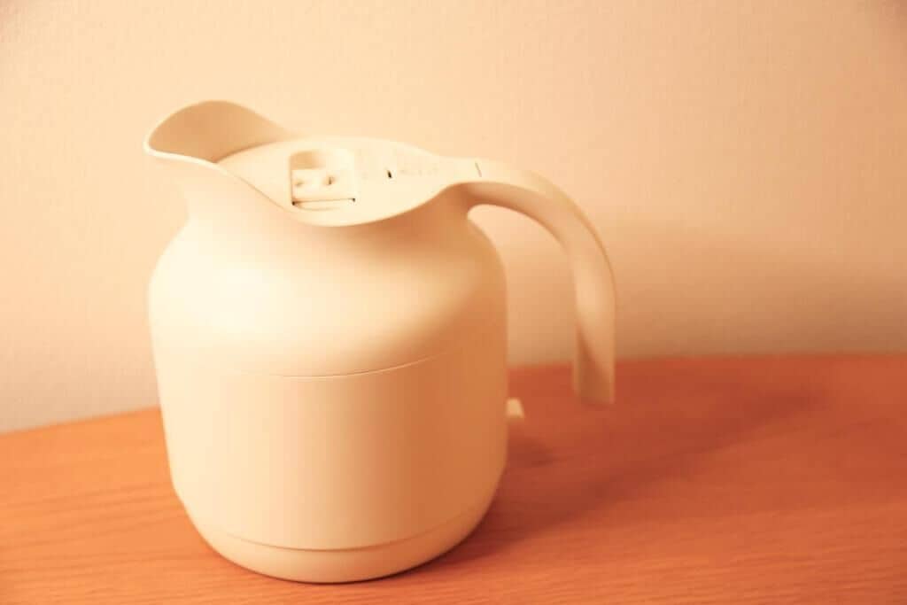 A white, modern, ceramic pitcher with a handle on a wooden surface.