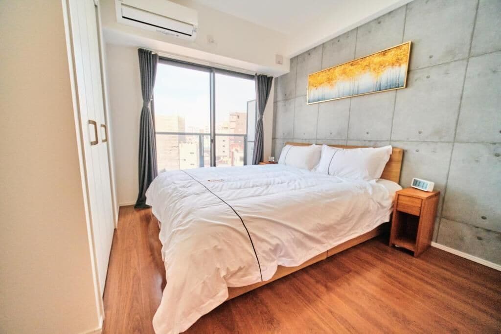 Une chambre à coucher avec un grand lit, une table de chevet, un tableau au mur et une fenêtre avec des rideaux.