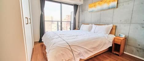 Une chambre à coucher avec un grand lit, une table de chevet, un tableau au mur et une fenêtre avec des rideaux.