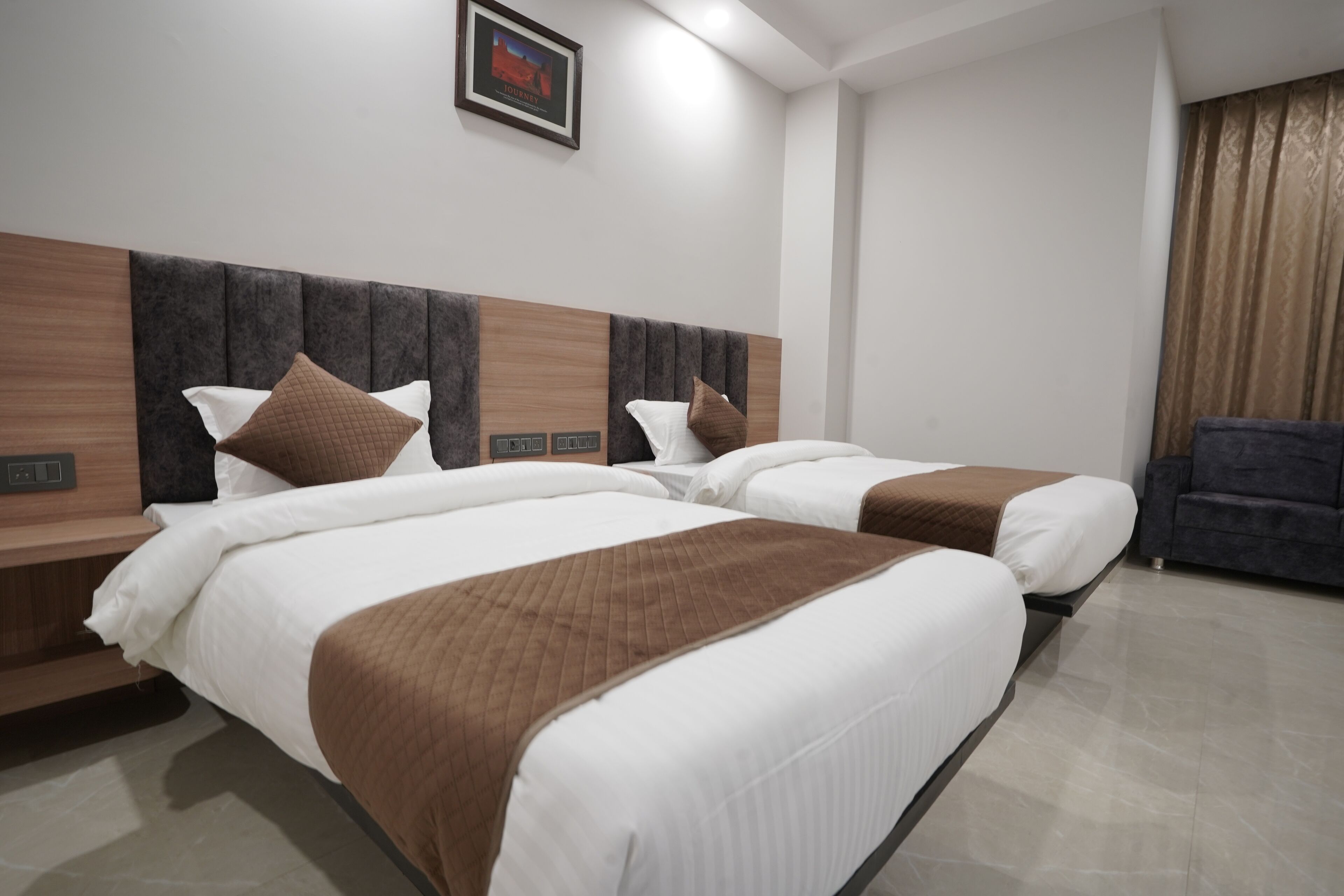 A hotel room with two beds, a wooden headboard, a framed picture on the wall, and a dark-colored armchair.