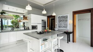 A modern kitchen with white cabinetry, a central island with bar stools, pendant lighting, and a large window with a view of greenery.