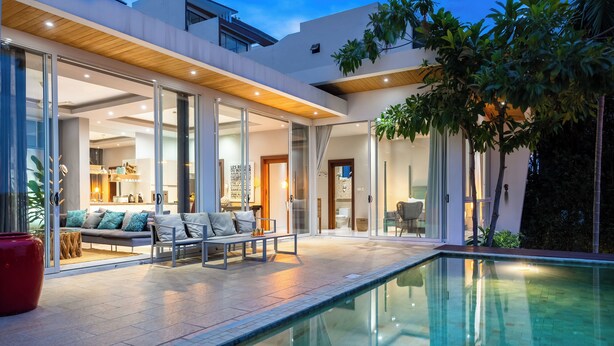 A modern house with a swimming pool, a dining area, and a living room with a sofa and chairs.