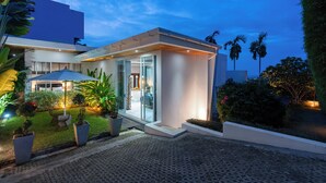 A modern house with a glass door entrance, a covered patio with a table and chairs, and a well-maintained garden with potted plants.