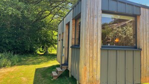 A wooden cabin with a large window, a small porch, and a staircase leading up to the entrance. - Lescargoterie de la Forge - Immersion Champêtre (Uzemain)