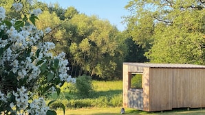 A small wooden cabin with a window, surrounded by a grassy field and dense trees. - Lescargoterie de la Forge - Immersion Champêtre (Uzemain)
