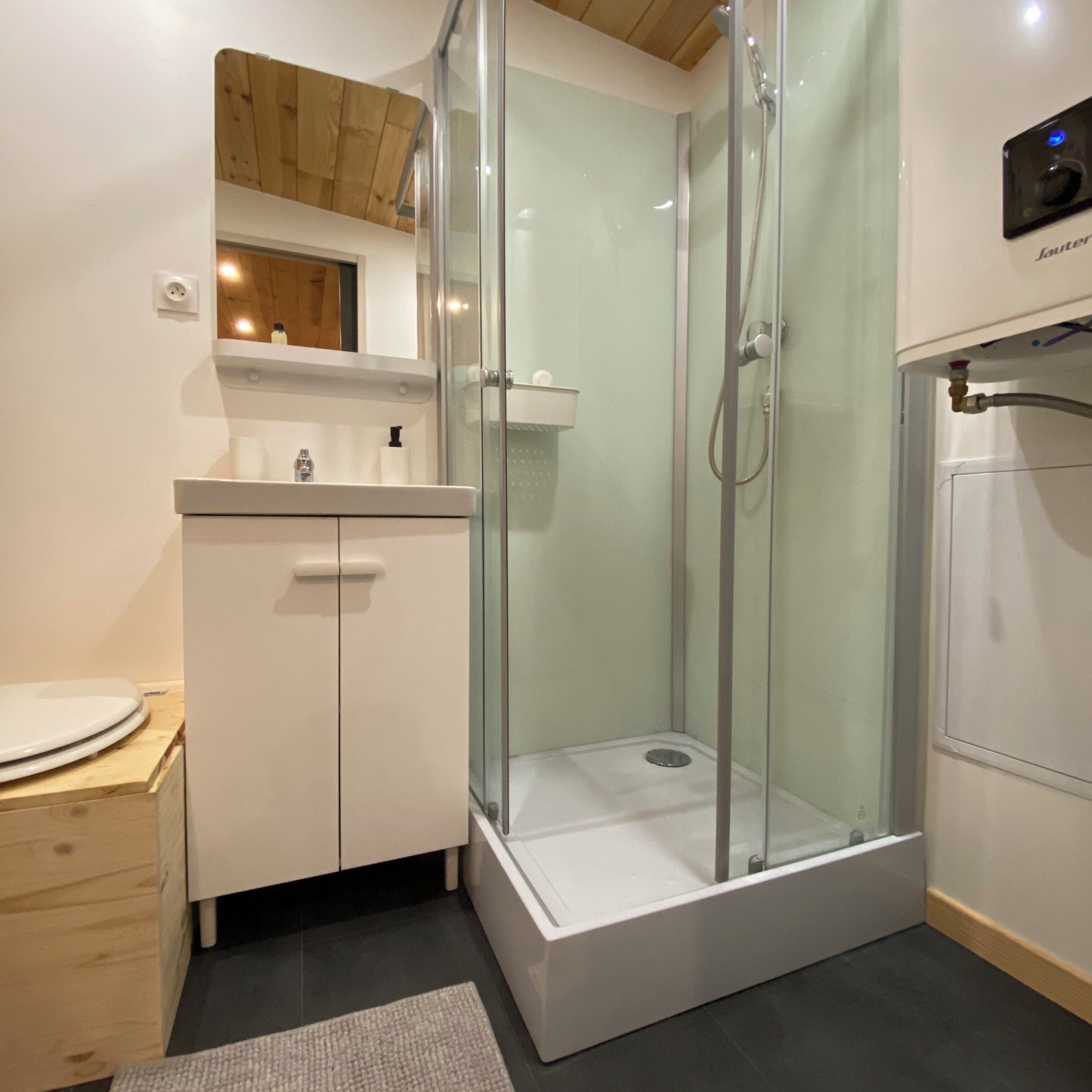 A modern bathroom with a glass-enclosed shower, a white sink with a mirror above it, and a wooden cabinet below.