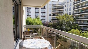 Un balcone con tavolo e sedie, un tavolo coperto e vista su edifici e vegetazione circostanti.