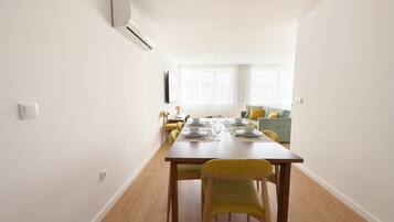 Un comedor moderno con una mesa de madera dispuesta para cuatro, sillas amarillas, un sofá verde y un equipo de aire acondicionado blanco en la pared.