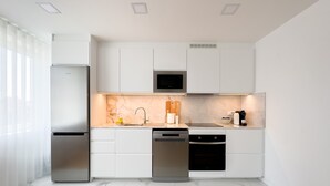 A modern kitchen with white cabinets, a stainless steel refrigerator, a microwave, a sink, and a dishwasher. - Vibrant Host-Campo 24  (Porto)