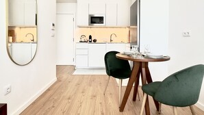 A modern kitchen with white cabinets, a microwave, and a dining area with two chairs and a round table. - Vibrant Host-Campo 24  (Porto)