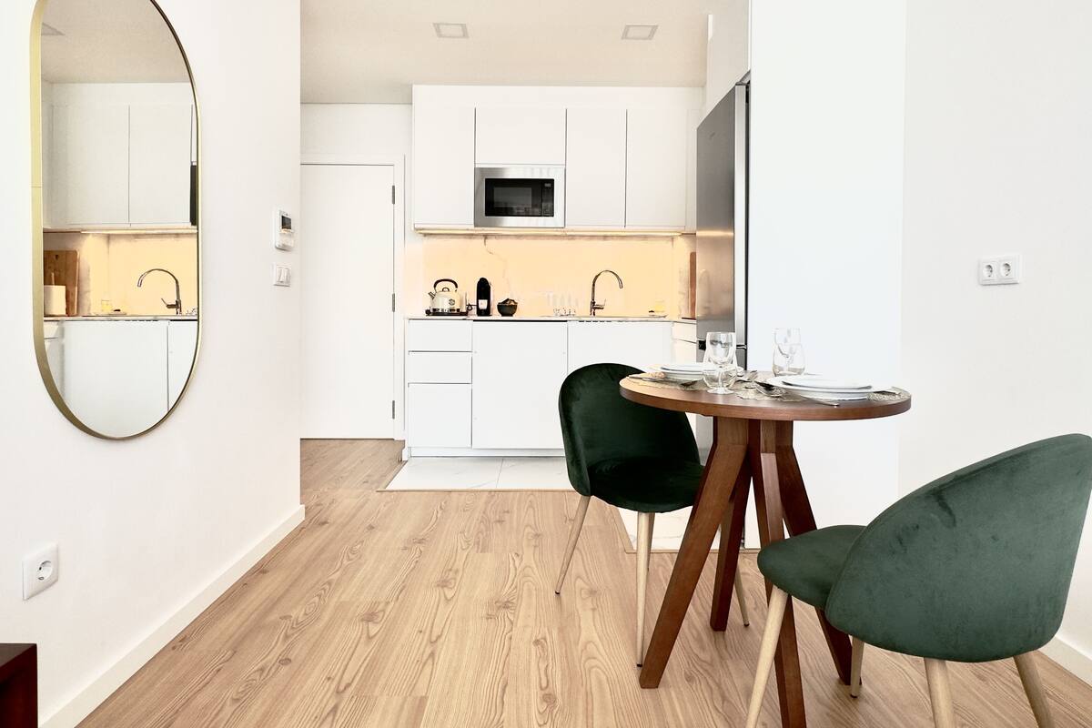 Une cuisine moderne avec des meubles blancs, un four à micro-ondes et un coin repas comprenant deux chaises et une table ronde.