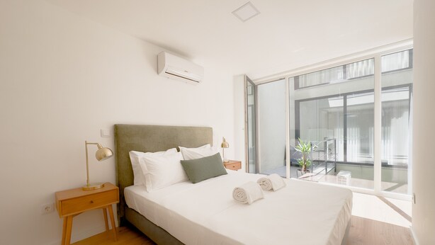 A modern bedroom with a large bed, a nightstand, a lamp, and a window with a view of the outside. - Vibrant Host-Campo 24  (Porto)
