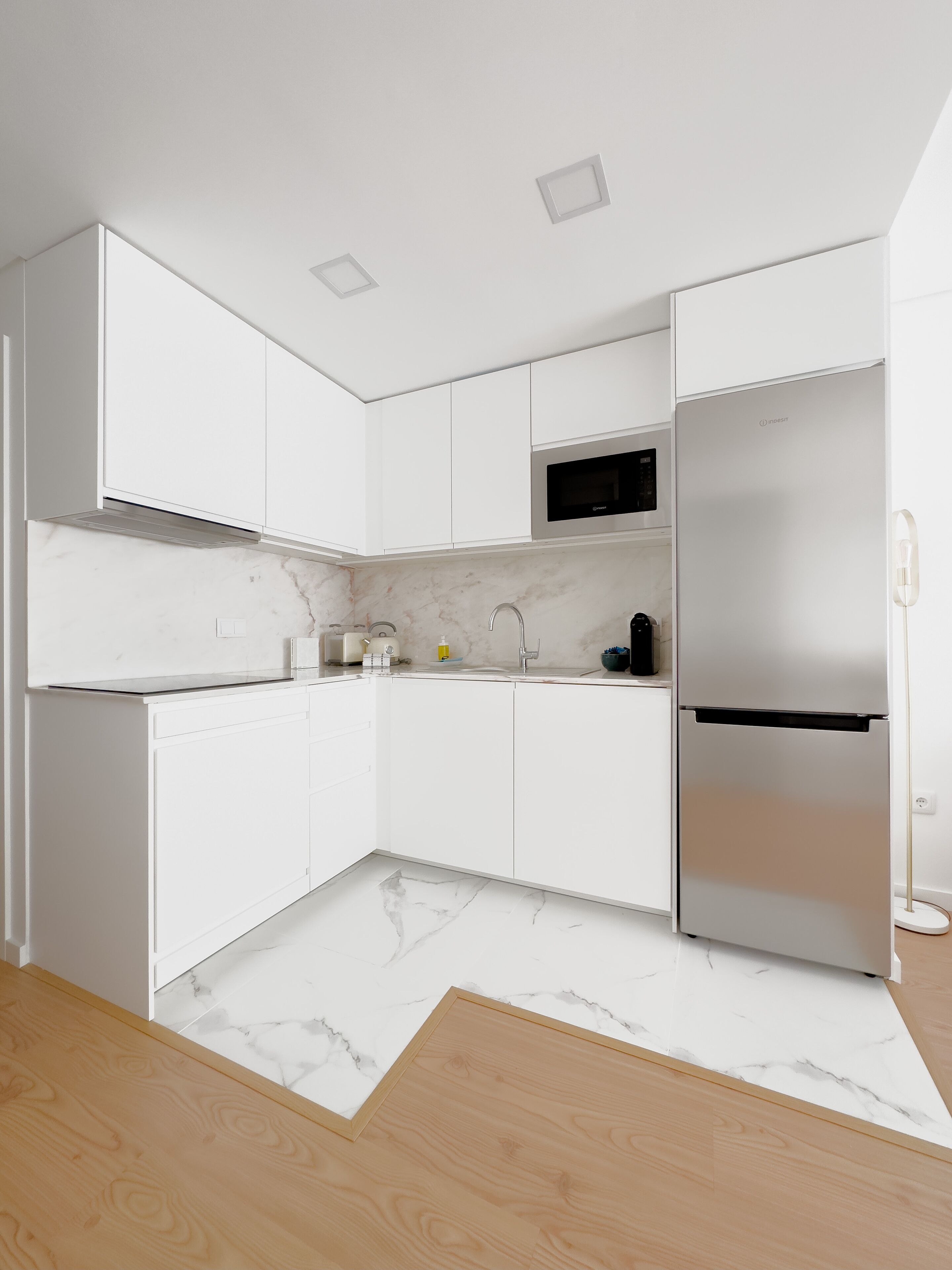 A modern kitchen with white cabinetry, a built-in microwave, and a stainless steel refrigerator.