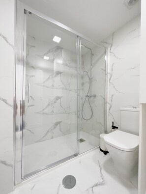 Une salle de bain moderne avec une douche à parois de verre, des murs en marbre blanc et des toilettes blanches.
