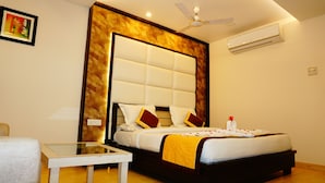 Quarto de hotel com uma cama grande, uma mesa de vidro, um ventilador de teto e um aparelho de ar condicionado.