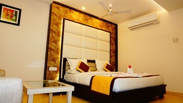 Una habitación de hotel con una cama grande, una mesa de vidrio, un ventilador de techo y un equipo de aire acondicionado.