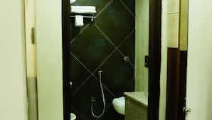 Casa de banho com parede revestida a mosaicos escuros, sanita branca, lavatório com espelho e zona de duche.