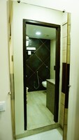 Un baño con pared de azulejos oscuros, inodoro blanco, lavamanos con espejo y zona de ducha.