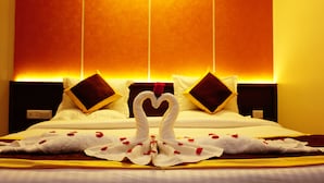 Quarto de hotel com cama, almofadas e arranjo decorativo de toalhas e rosas.