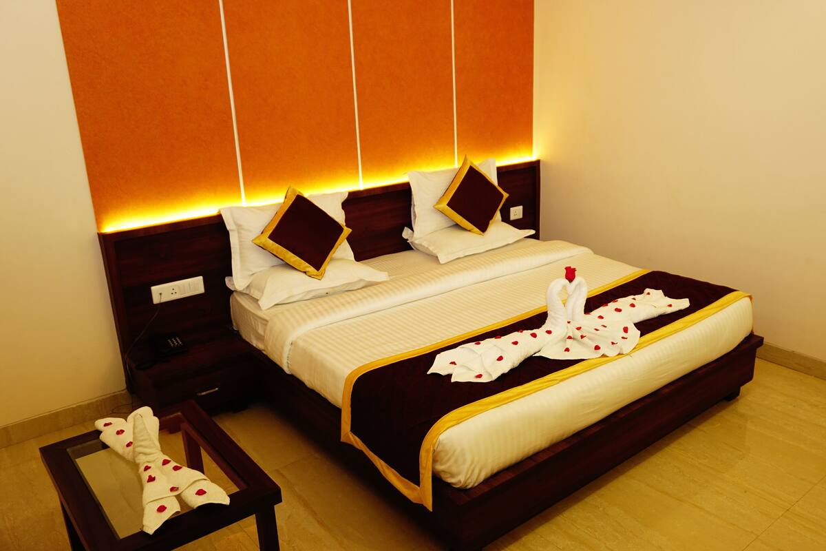 Cama bem arrumada com lençóis brancos, toalha decorativa em formato de cisne e cabeceira de madeira com luz embutida.