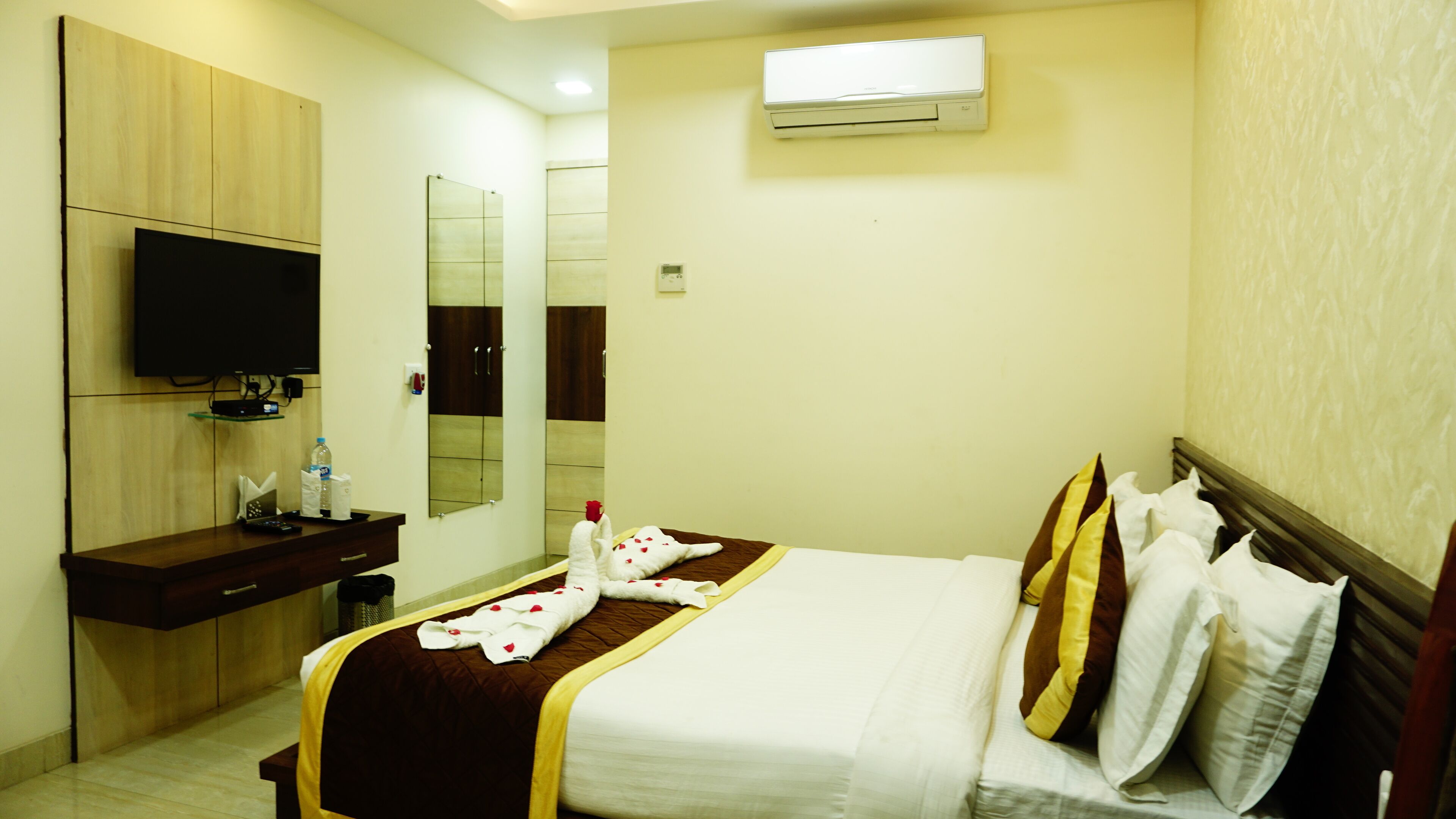 A hotel room with a bed, a TV, a mirror, a wardrobe, and an air conditioning unit.