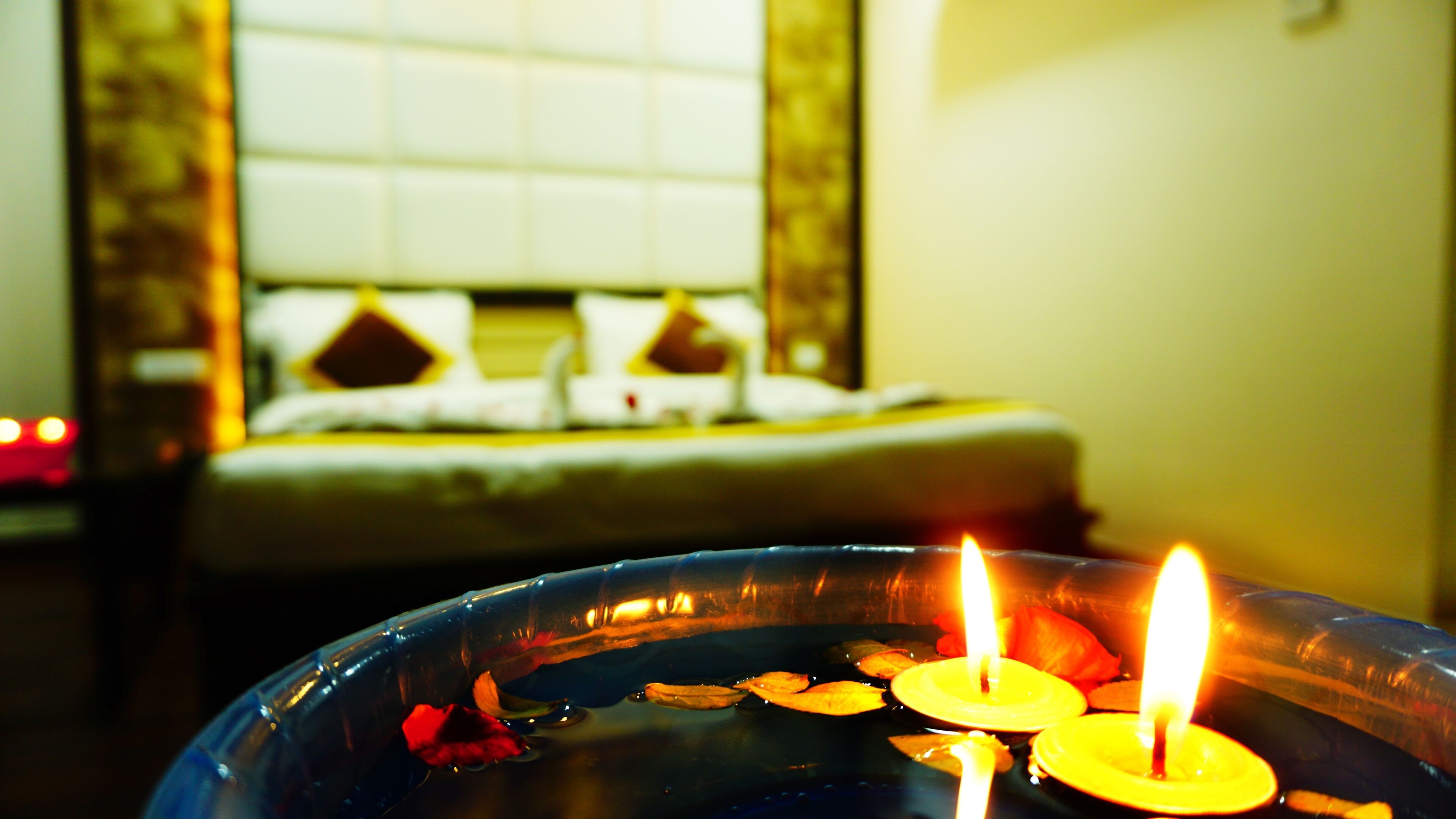 A room with a bed in the background and a bowl of water with two lit candles in the foreground.