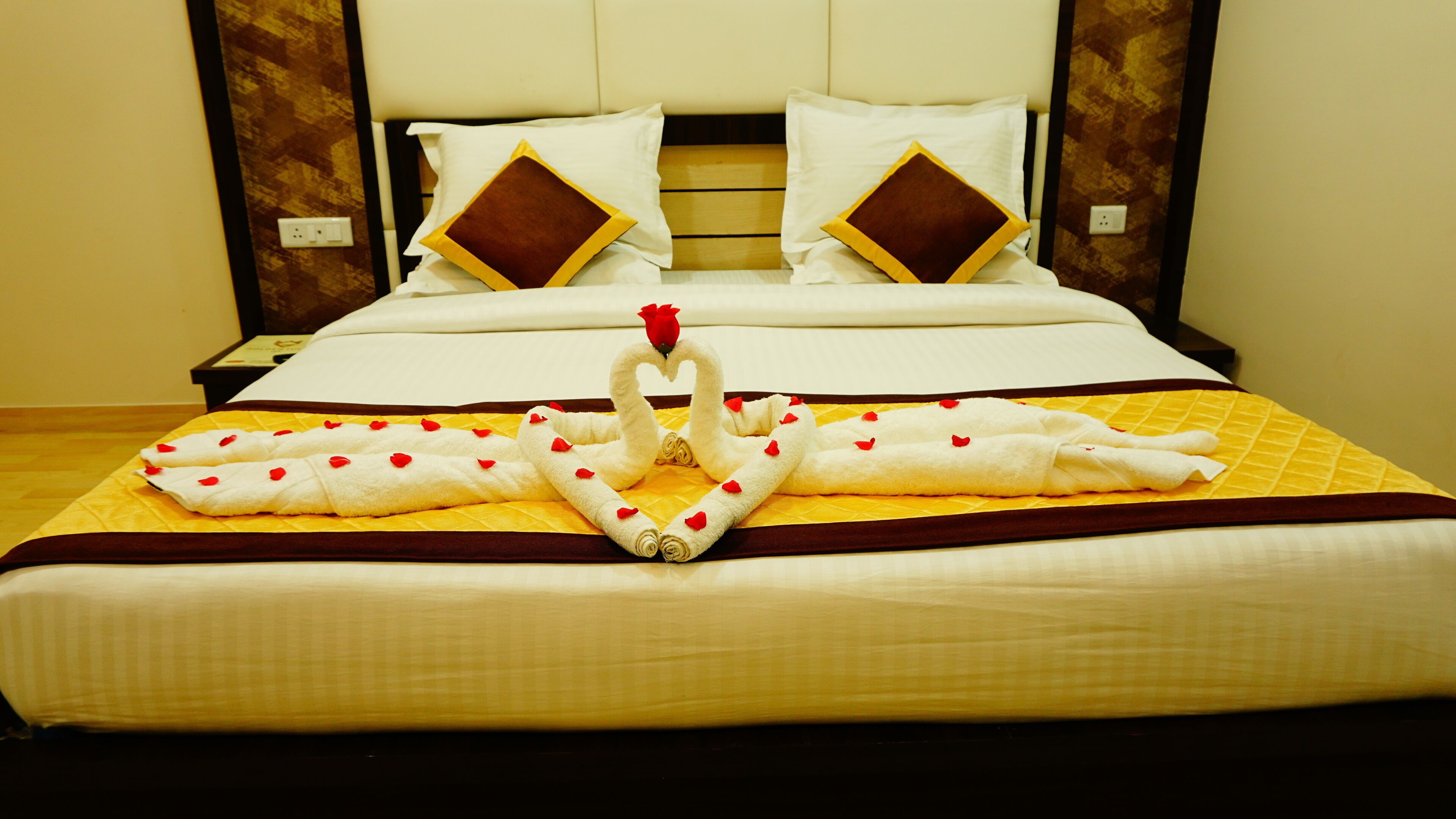 A hotel room with a neatly made bed, a wooden headboard, and a yellow bedspread.