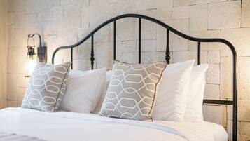 Een bed met een witte matras en twee gestreepte kussens, een zwart metalen hoofdbord en een muur met een reliëf stenen patroon.