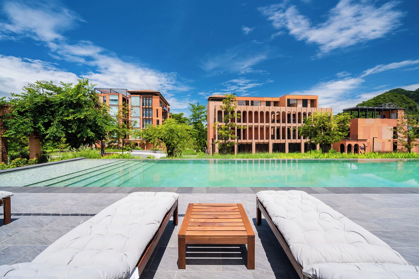 Um hotel moderno com área de piscina, espreguiçadeiras e uma mesa de madeira.
