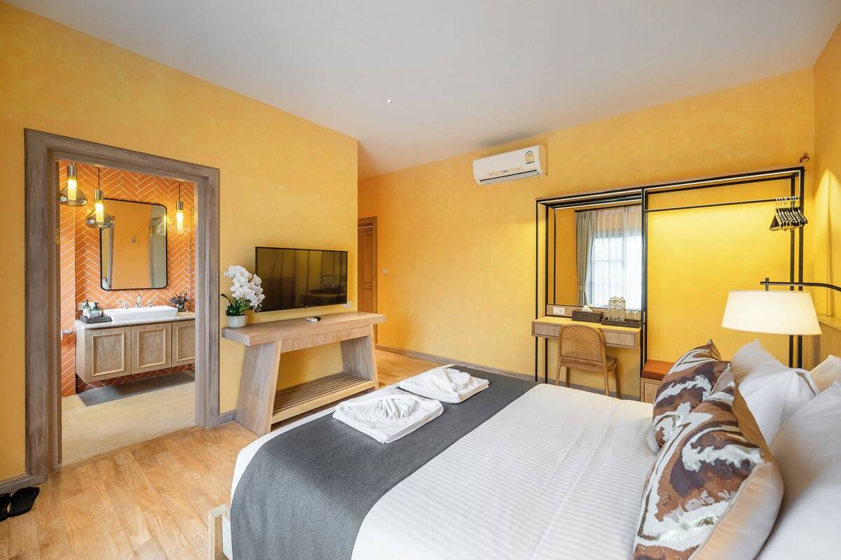 A hotel room with a bed, a desk with a TV, a mirror, and a bathroom with a sink and shower.